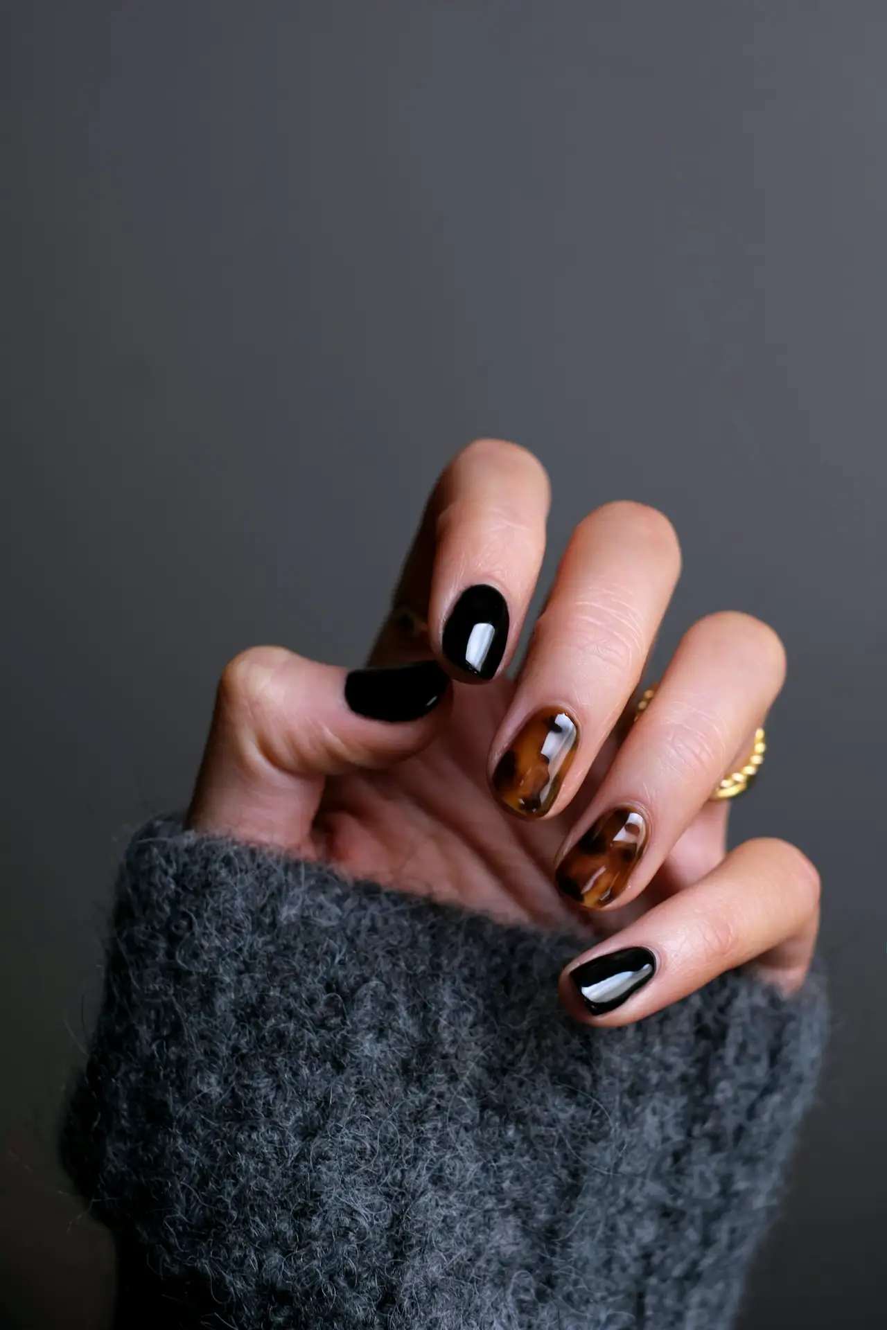 Hand with glossy black and tortoiseshell nails against a grey sweater